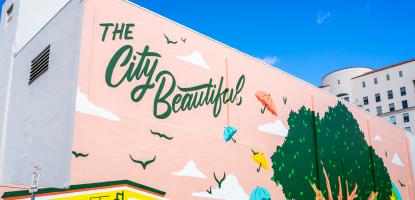 blue sky in the background, a pink mural at Mcbride Plaza depicting a large tree with umbrellas and birds and a trolley
